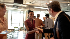 Diverse group of professionals networking at a business event, shaking hands and exchanging business cards to build client relationships.